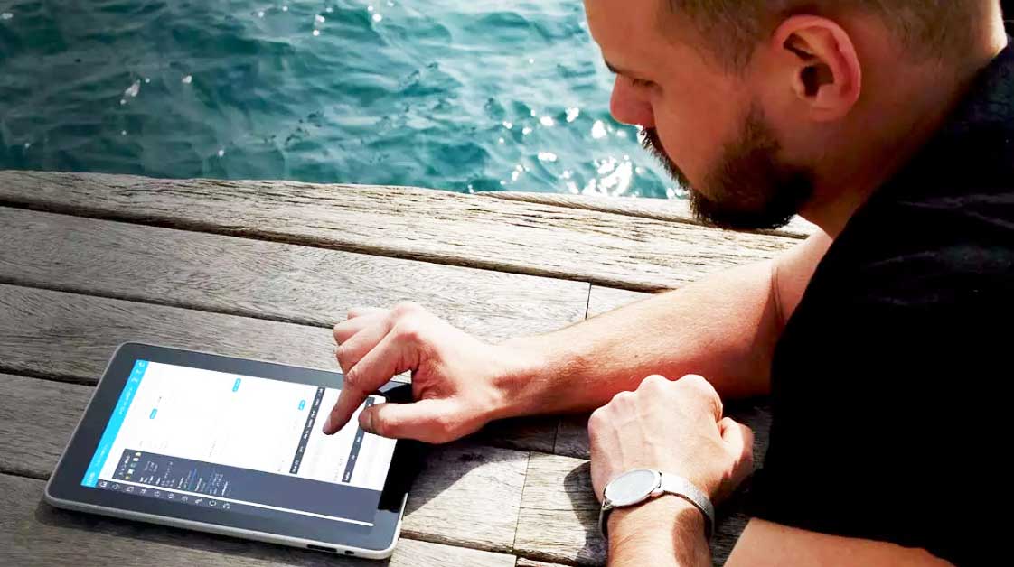 man sitting on dock next to water, looking at a tablet