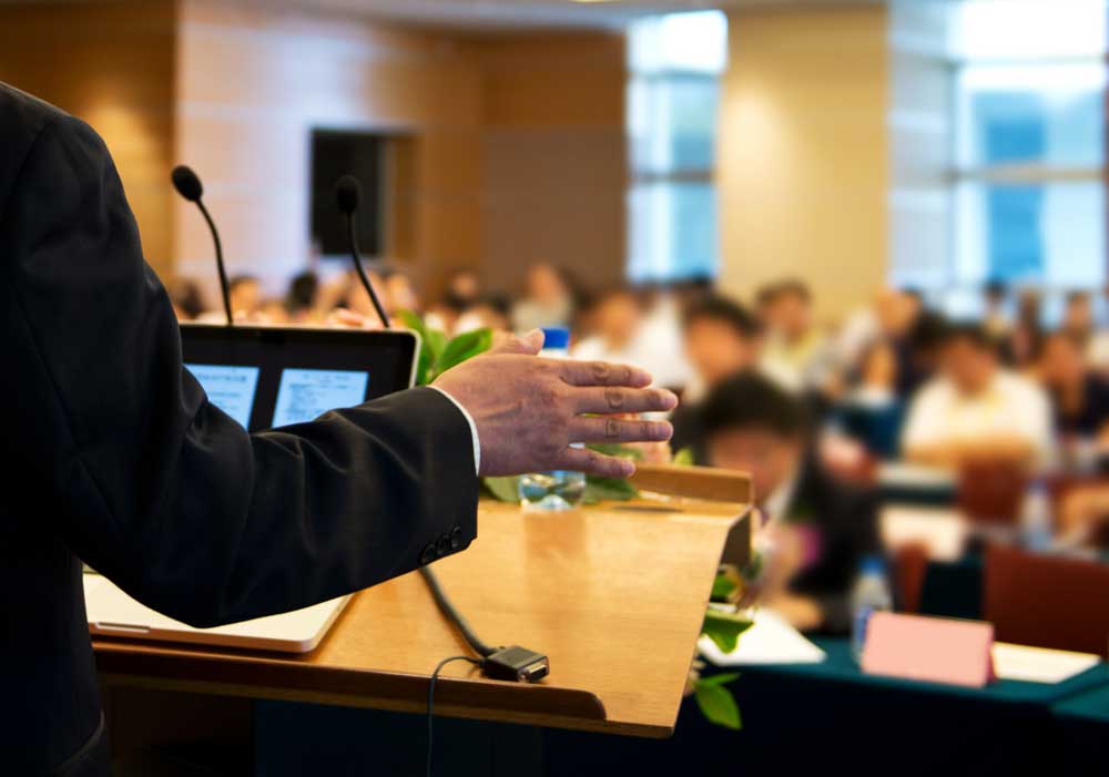 person standing behind podium speaking to room