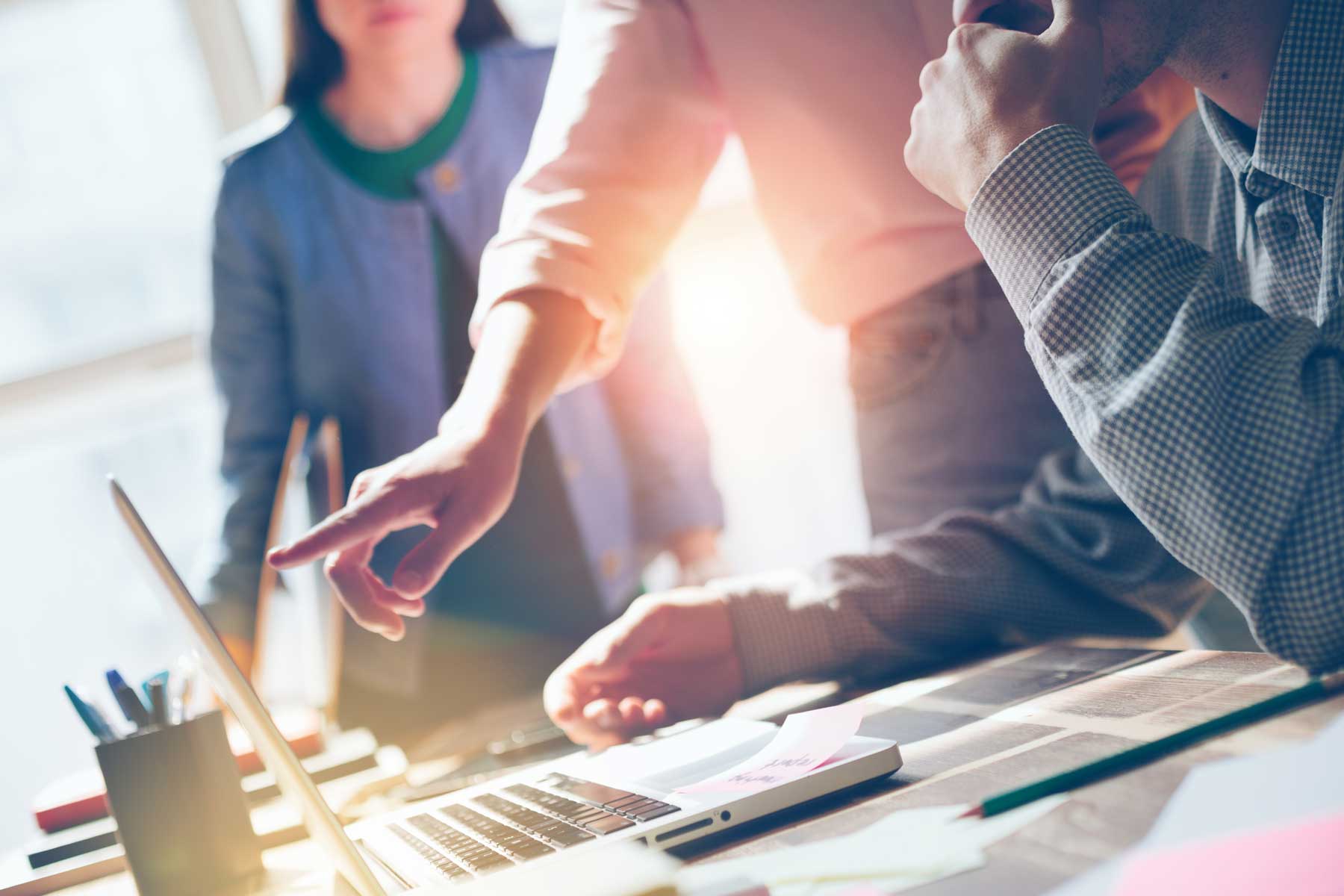 man pointing to a computer screen while two colleagues look on